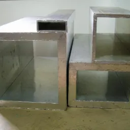 Dwa izolowane, prostokątne kanały wentylacyjne o różnych rozmiarach, ustawione obok siebie na jasnej powierzchni. Widoczne wewnętrzne ścianki i metaliczna izolacja zewnętrzna.