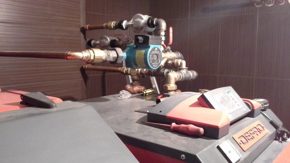 Instalacja grzewcza z pompą obiegową, rurami miedzianymi i zaworami, zamontowana na kotle grzewczym, z widocznymi narzędziami monterskimi na powierzchni kotła.