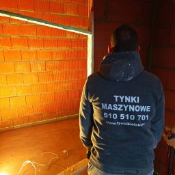 Tynki Bielsko Łukasz Kiecza - Wnętrze w trakcie prac murarskich z widocznym laserowym niwelatorem oraz pracownikiem w bluzie z nadrukiem firmowym