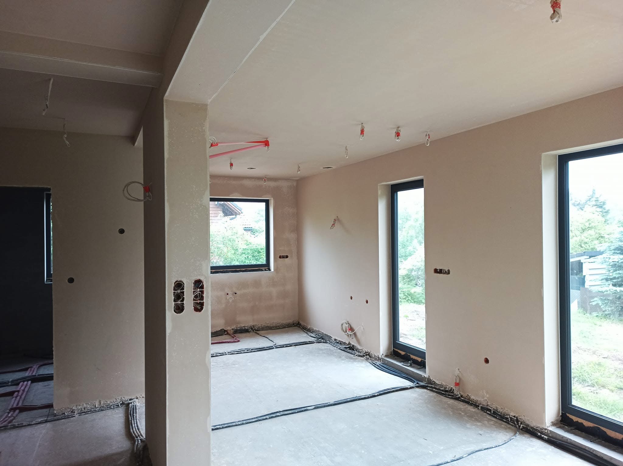 Surowe wnętrze po nałożeniu gładzi gipsowej, widoczne instalacje elektryczne i grzewcze w podłodze, przygotowane do dalszych prac wykończeniowych.