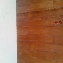 Fragment ściany w Opatowie: połączenie białego tynku strukturalnego i paneli imitujących drewno. Widoczne otwory na gniazdka elektryczne.