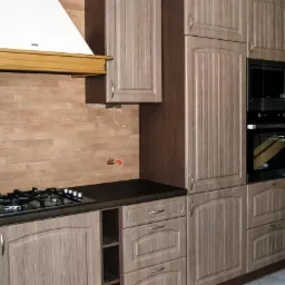 Kuchnia z zabudową w odcieniach beżu i brązu, z piekarnikiem, kuchenką gazową i wysuwaną szafką cargo. Fronty frezowane, okap w kolorze białym z drewnianą listwą.