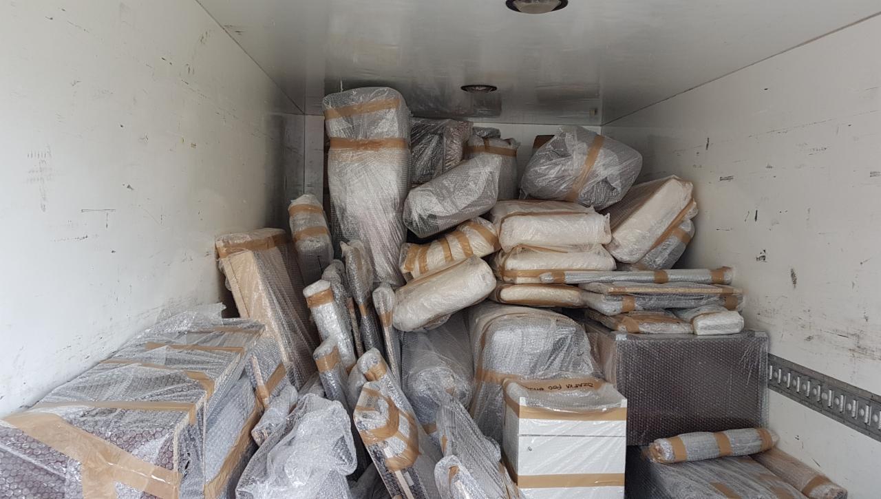 Wnętrze brudnej paki samochodu dostawczego wypełnione po brzegi meblami i kartonami zabezpieczonymi folią bąbelkową i taśmą klejącą, gotowymi do transportu.