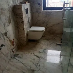 Nowoczesna łazienka wykończona marmurem, z podwieszaną toaletą i szklaną kabiną prysznicową.