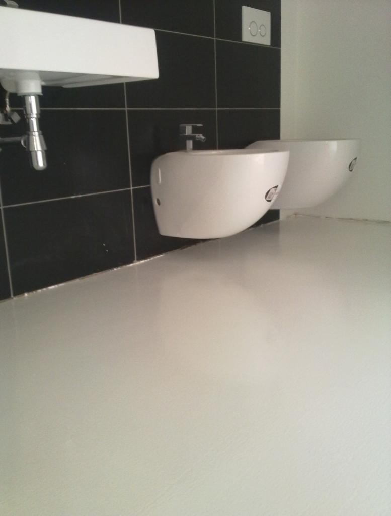 Nowoczesna łazienka z białą armaturą na tle czarnych płytek i jasnej podłogi. Minimalistyczny design z widocznym zlewem i bidetami.