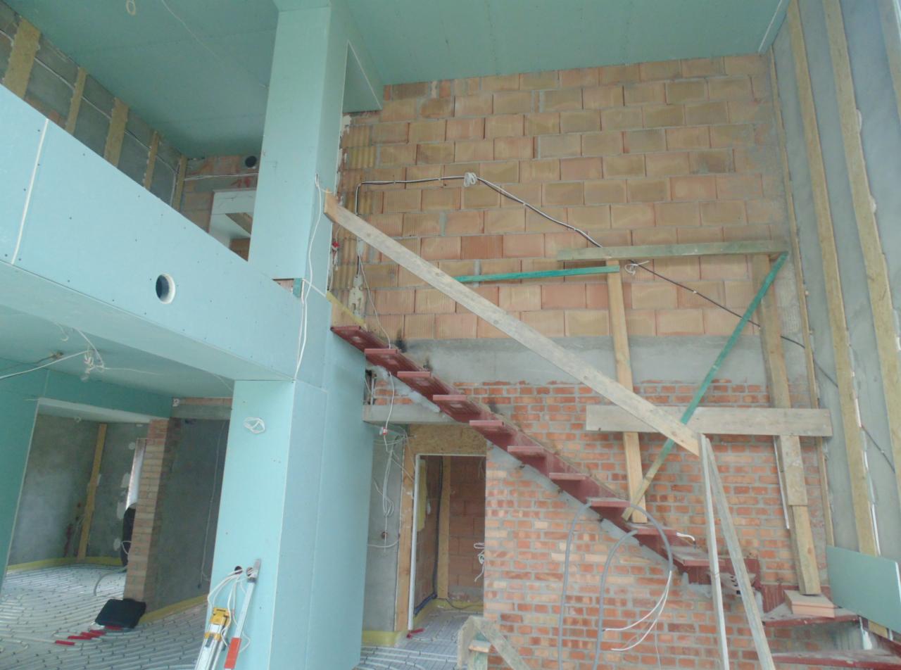 Wnętrze w trakcie remontu: ściany z płyt gipsowo-kartonowych pomalowane na niebiesko, częściowo odsłonięta cegła, prowizoryczne schody i instalacja ogrzewania podłogowego.