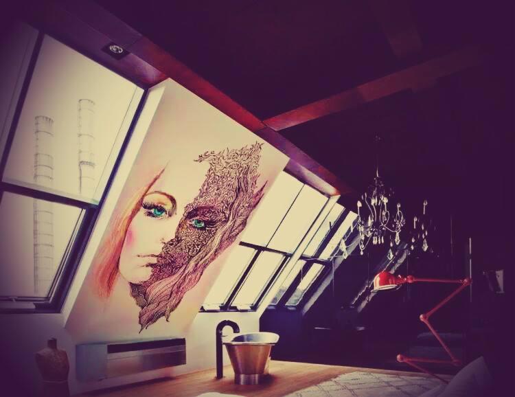 Artystyczna dekoracja ścienna z motywem twarzy w mansardzie z oknami dachowymi i żyrandolem. Część twarzy pokryta ornamentem, dodająca unikalnego charakteru.