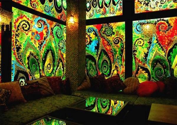 Kolorowe, abstrakcyjne malowidło ścienne z motywami roślinnymi w stylu paisley, oświetlone lampą, tworzące unikalną dekorację wnętrza.