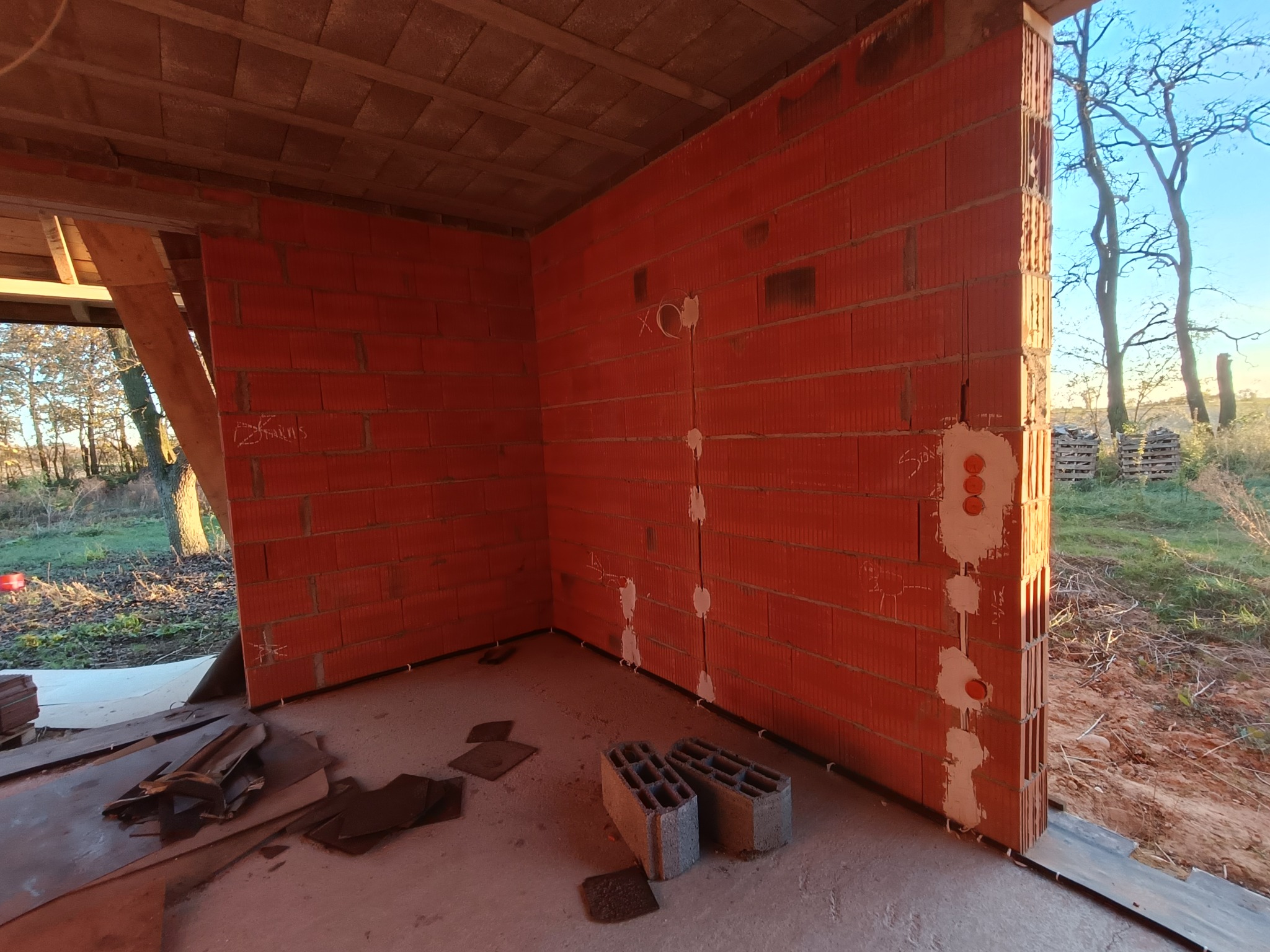 Wnętrze budynku w trakcie budowy, widoczne ściany z czerwonej cegły z wyżłobieniami na instalacje elektryczne i wyprowadzonymi przewodami w ścianie, nieotynkowane ściany, surowy strop, widok...