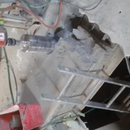 Wiertnica diamentowa Hilti w trakcie wiercenia rdzeniowego w stropie betonowym, widoczna drabina aluminiowa, odkurzacz przemysłowy i czerwone wiadro na odpady.