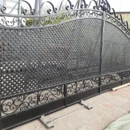 Nowa, czarna, dwuskrzydłowa brama z kutymi zdobieniami w stylu retro, leżąca na betonowym podłożu, przed montażem.