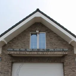 Detale wykończenia podbitki dachowej na budynku z cegły klinkierowej, widoczne okno, białe elementy wykończeniowe i fragment dachu z czarną dachówką.