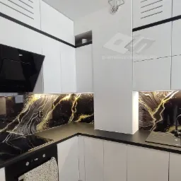 Kuchnia z białymi szafkami i czarnym panelem szklanym z motywem marmuru i złotych żył, oświetlonym listwą LED.