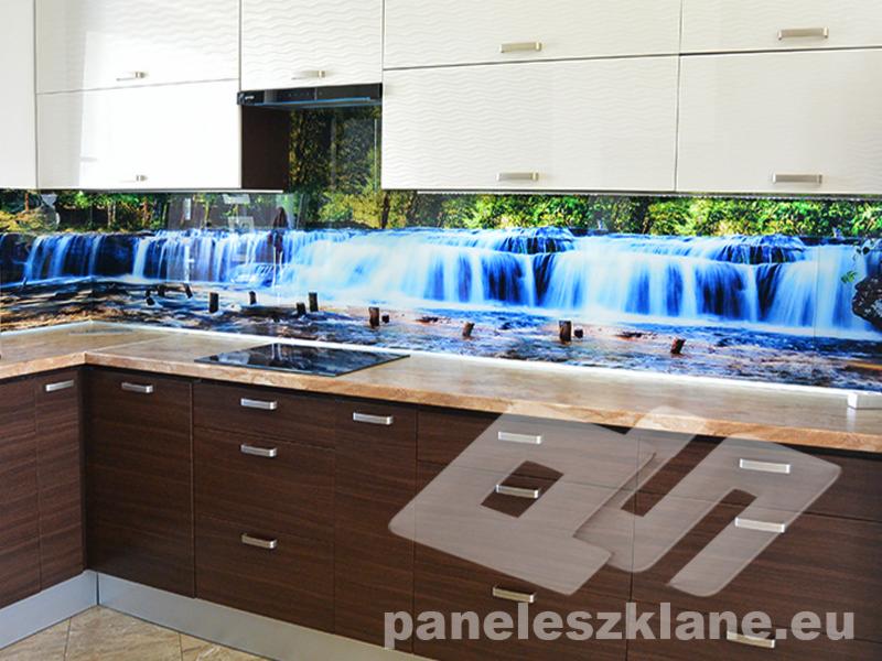 Szklany panel kuchenny z motywem wodospadu, zamontowany między szafkami górnymi i blatem, z widocznym logo firmy na dolnej części.
