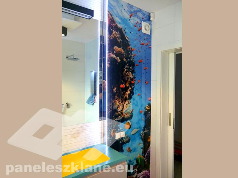 Szklana ściana w łazience z podświetlanym motywem rafy koralowej, widoczny fragment prysznica i przesuwne drzwi.