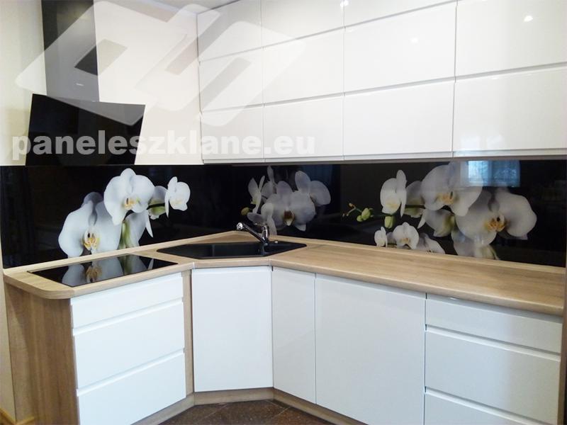 Biała kuchnia z czarnym szklanym panelem nad blatem, zdobionym motywem białych orchidei.