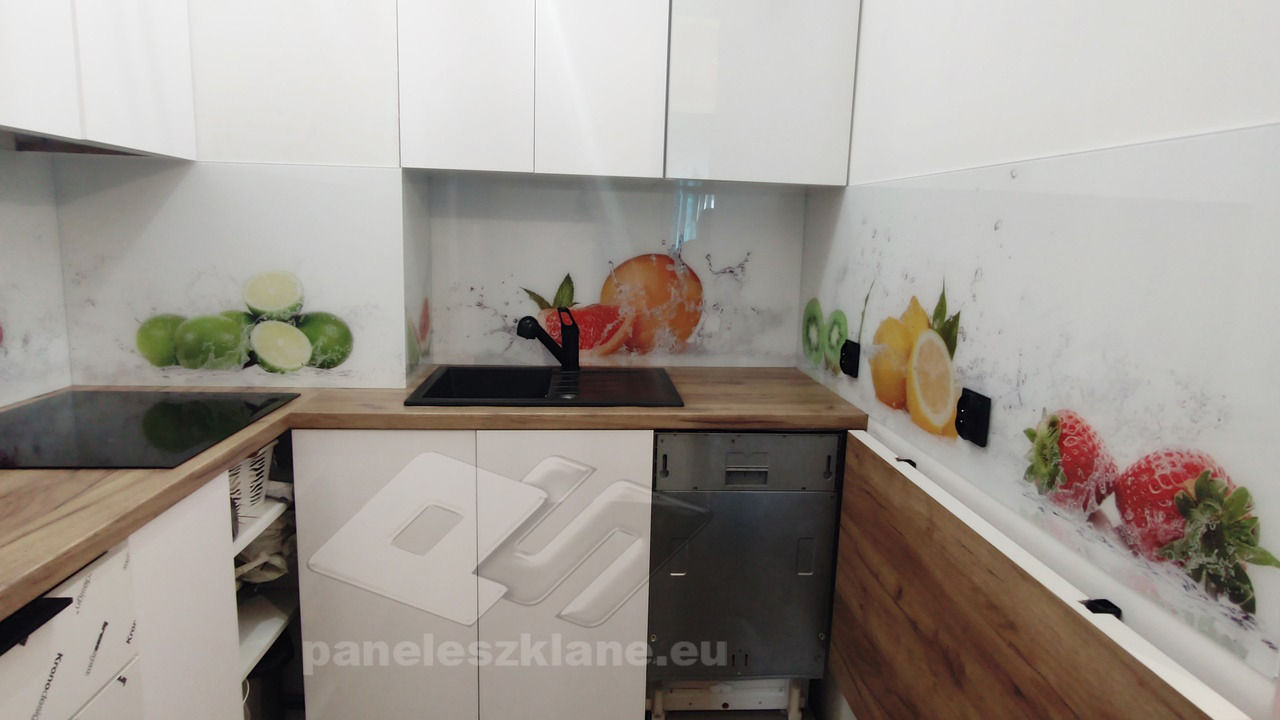 Szklany panel kuchenny z motywem owoców: limonki, grejpfruty, kiwi, cytryny i truskawki, zamontowany nad blatem i zlewem w białej kuchni.