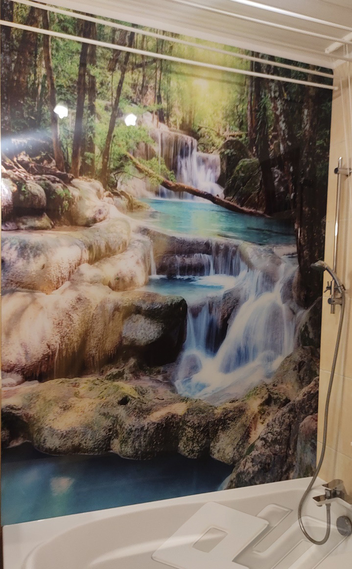 Fototapeta z motywem wodospadu w łazience nad wanną, widoczny fragment baterii i suszarka na pranie pod sufitem.