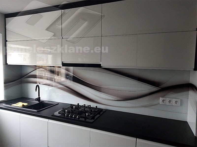 Nowoczesna kuchnia z białymi szafkami i czarnym blatem, panel szklany z abstrakcyjnym wzorem nad blatem, czarny zlew i płyta gazowa.
