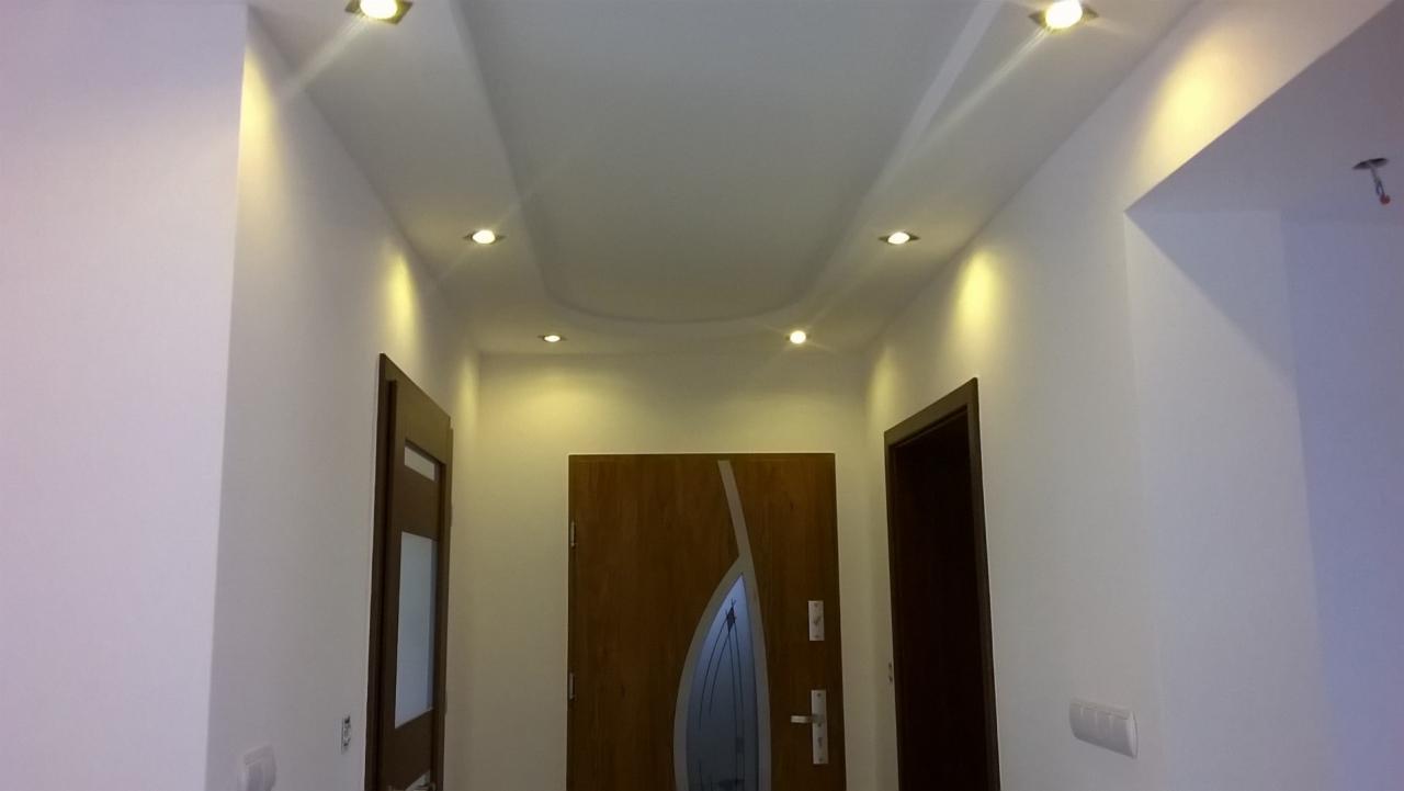 Korytarz po remoncie z dwiema parami drzwi, oświetleniem punktowym w suficie podwieszanym i świeżo pomalowanymi ścianami na biało.