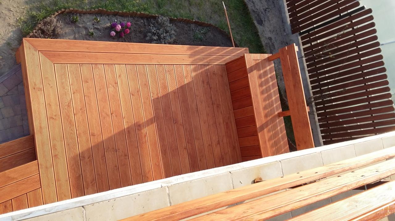 Drewniany taras z desek, widok z góry, z elementami ogrodu i ogrodzenia. Ciepłe oświetlenie podkreśla strukturę drewna.