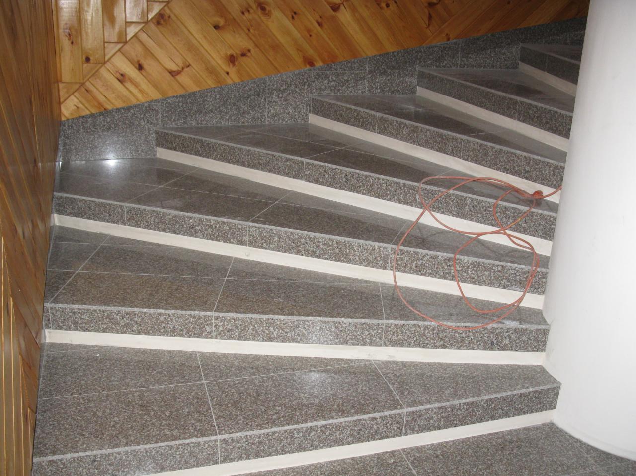 Wykończone schody z szarego, nakrapianego gresu z białymi wstawkami, drewniana boazeria na ścianie i zwisający kabel. Widok z dołu.