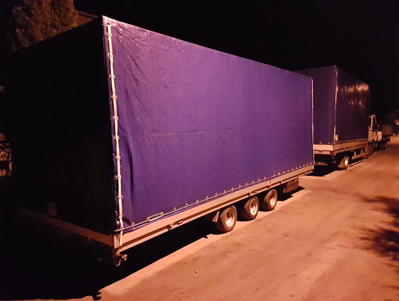 Ciężarówki z naczepami pod plandekami zaparkowane nocą, widoczne trzy osie naczepy i plandeka w kolorze fioletowym.