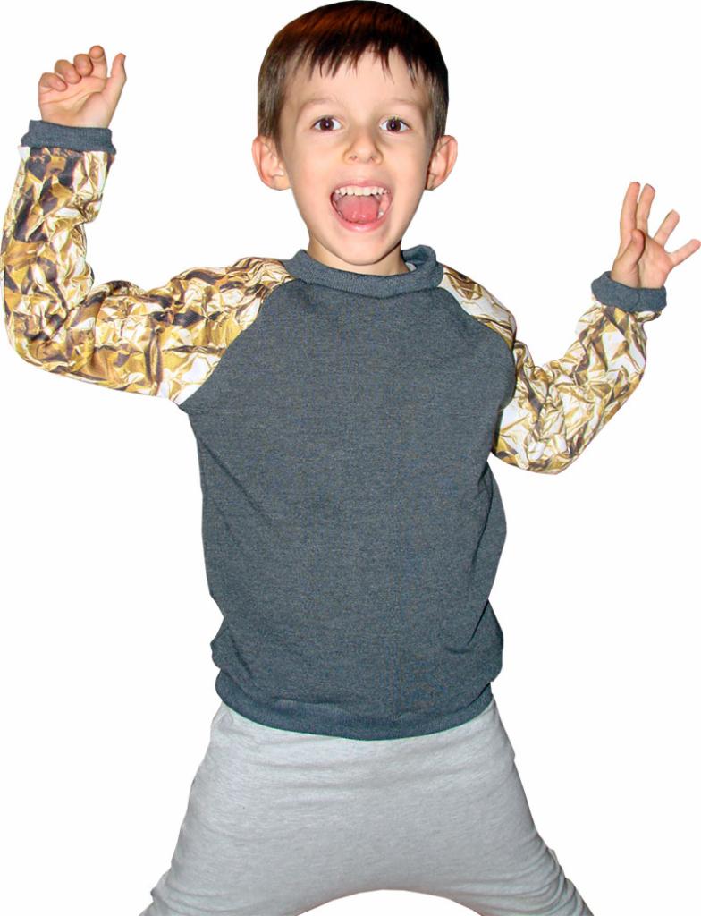 Uśmiechnięty chłopiec w szaro-złotej bluzie z długim rękawem, w dynamicznej pozie z uniesionymi rękami na białym tle.