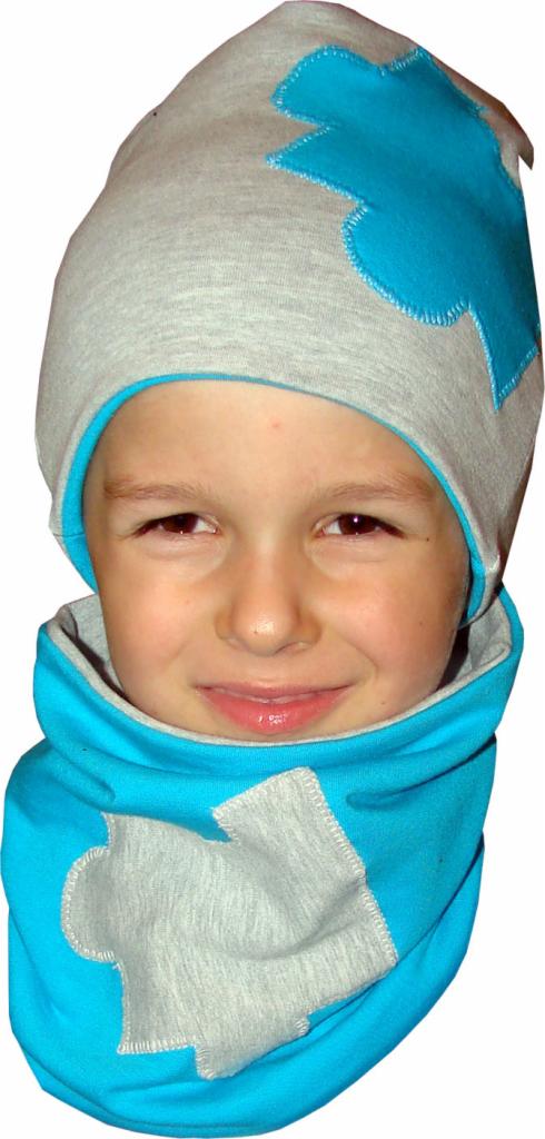 Uśmiechnięty chłopiec w szaro-turkusowym komplecie: czapka z aplikacją i komin. Widoczne szwy i detale wykończenia. Całość na białym tle.