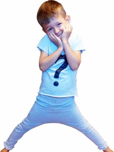 Uśmiechnięty chłopiec w jasnoniebieskiej piżamie z dużym znakiem zapytania, pozuje z rękami przy twarzy, stojąc w rozkroku na białym tle.