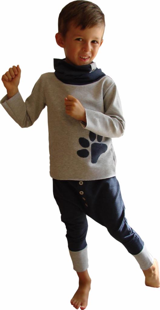 Chłopiec w szarej bluzce z łapą i ciemnych spodniach typu baggy z mankietami, prezentujący gotowy strój. Uśmiechnięty, pozuje na białym tle.