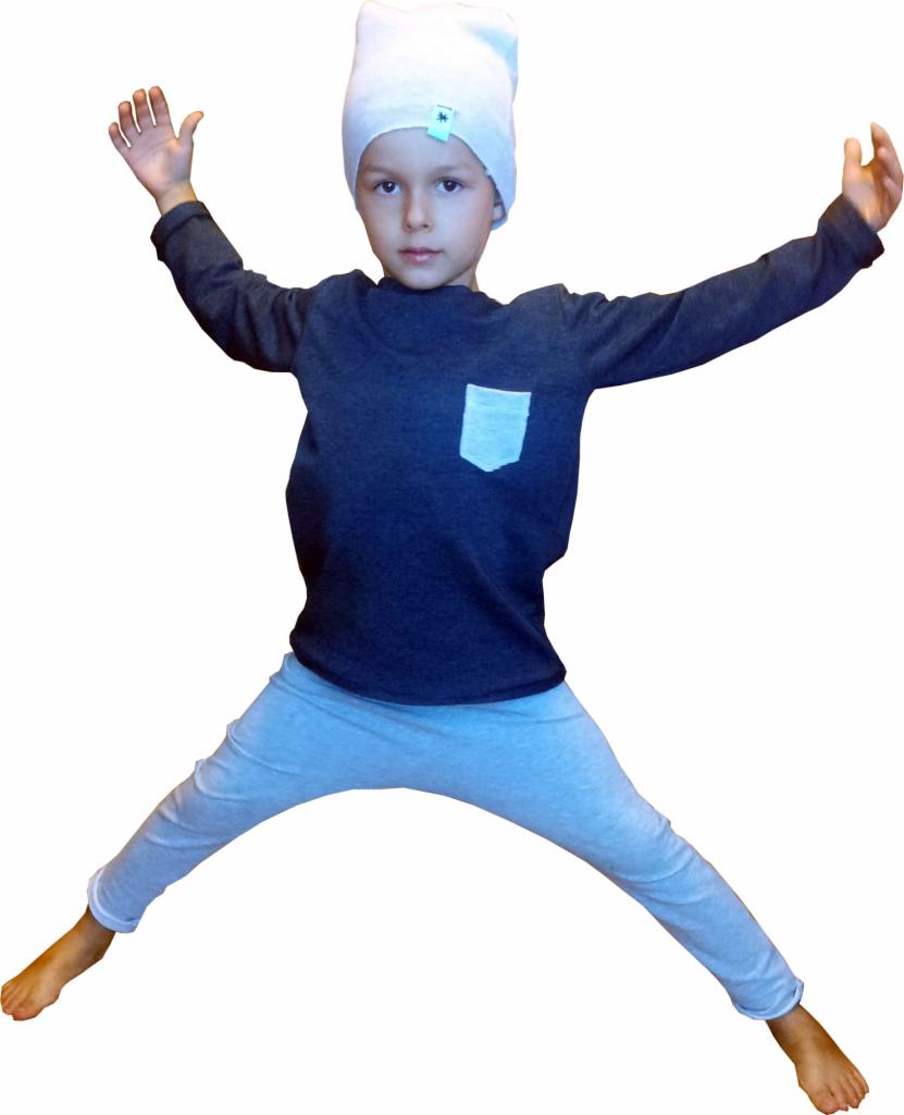 Radosny chłopiec w szarej bluzie z kieszonką, spodniach i białej czapce z gwiazdką, skacze na białym tle, prezentując odzież dziecięcą.