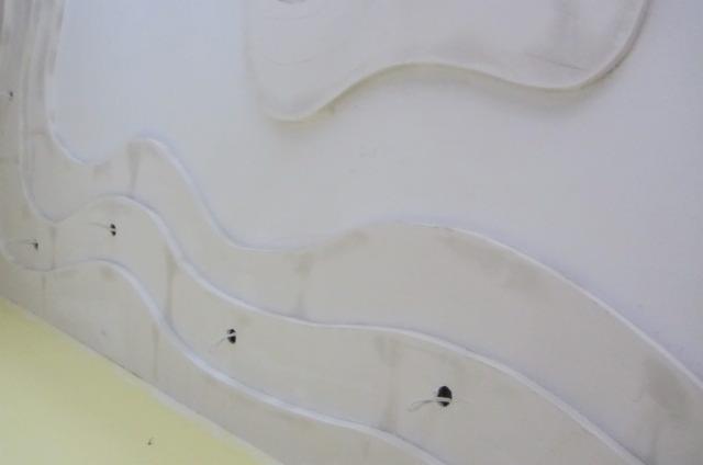 Biały sufit z dekoracyjnymi, falistymi elementami gipsowymi i otworami na oświetlenie, widziany pod kątem. Nowoczesny design wnętrza w trakcie wykończenia.