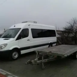 Biały bus Mercedes Sprinter z przyczepą platformową na zewnątrz, gotowy do transportu. Przyczepa z niskim najazdem ułatwia załadunek.