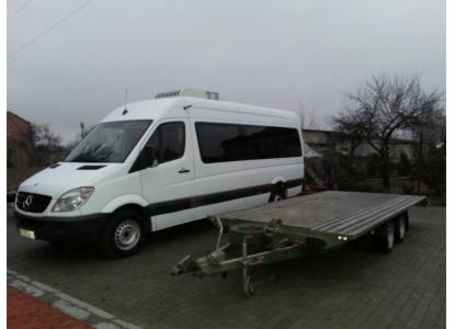 Biały bus Mercedes Sprinter z przyczepą platformową na zewnątrz, gotowy do transportu. Przyczepa z niskim najazdem ułatwia załadunek.