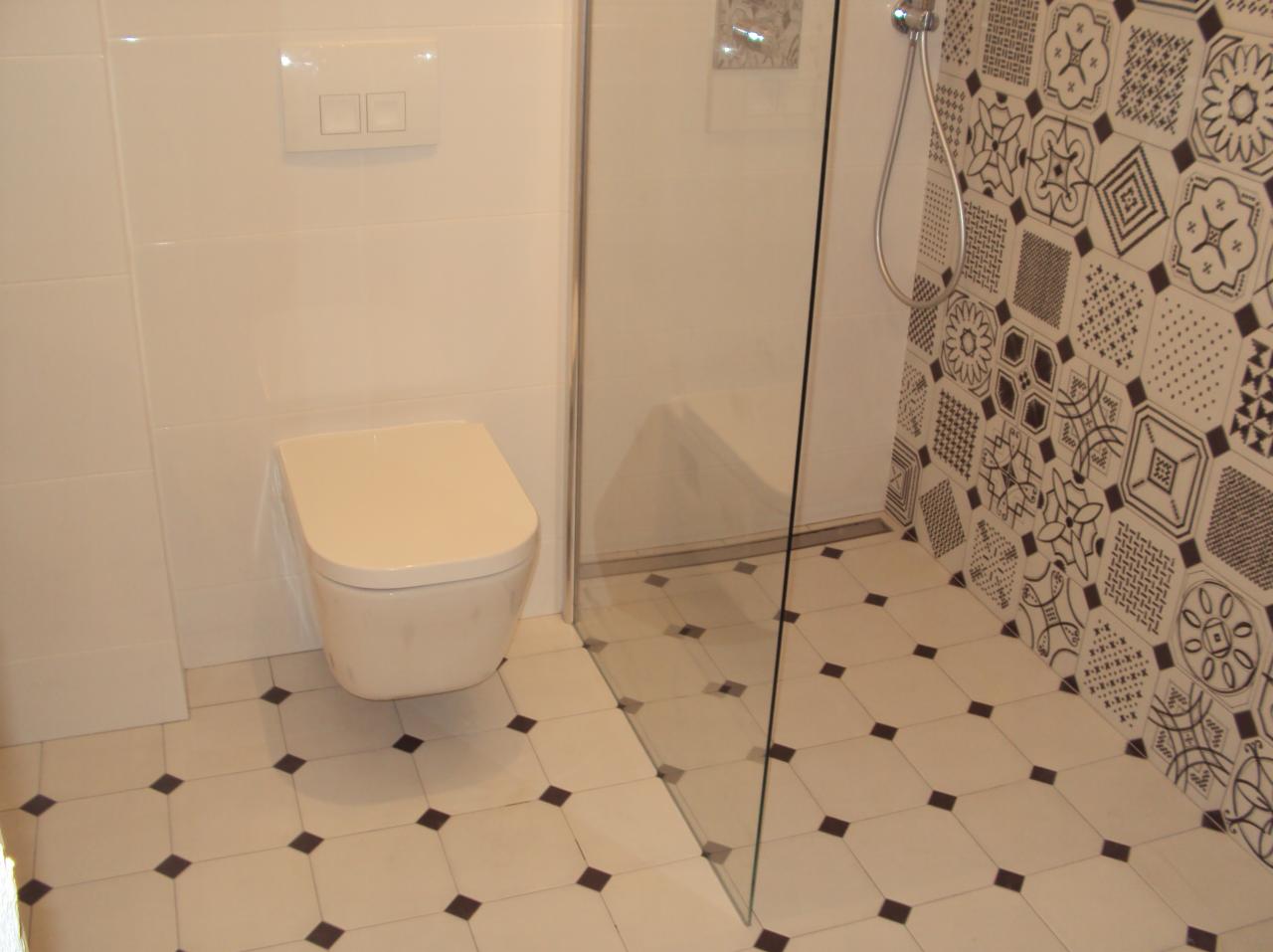 Nowoczesna łazienka z podwieszaną toaletą, kabiną prysznicową typu walk-in i biało-czarną mozaiką na ścianie. Minimalistyczny design z akcentem dekoracyjnym.