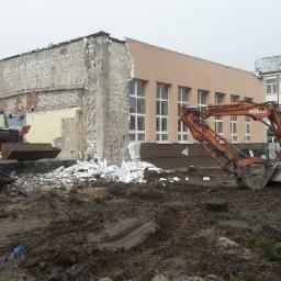 P.H.U. RAVI TRANS - Pomarańczowa koparka ATLAS 1504 i czerwony ładowacz teleskopowy pracują na placu budowy z gruzem, w tle budynki szkolne.