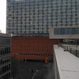 Pracownik w kasku, na linach, myje elewację budynku Elbphilharmonie w Hamburgu, widok z góry, w tle ulica i inne budynki.