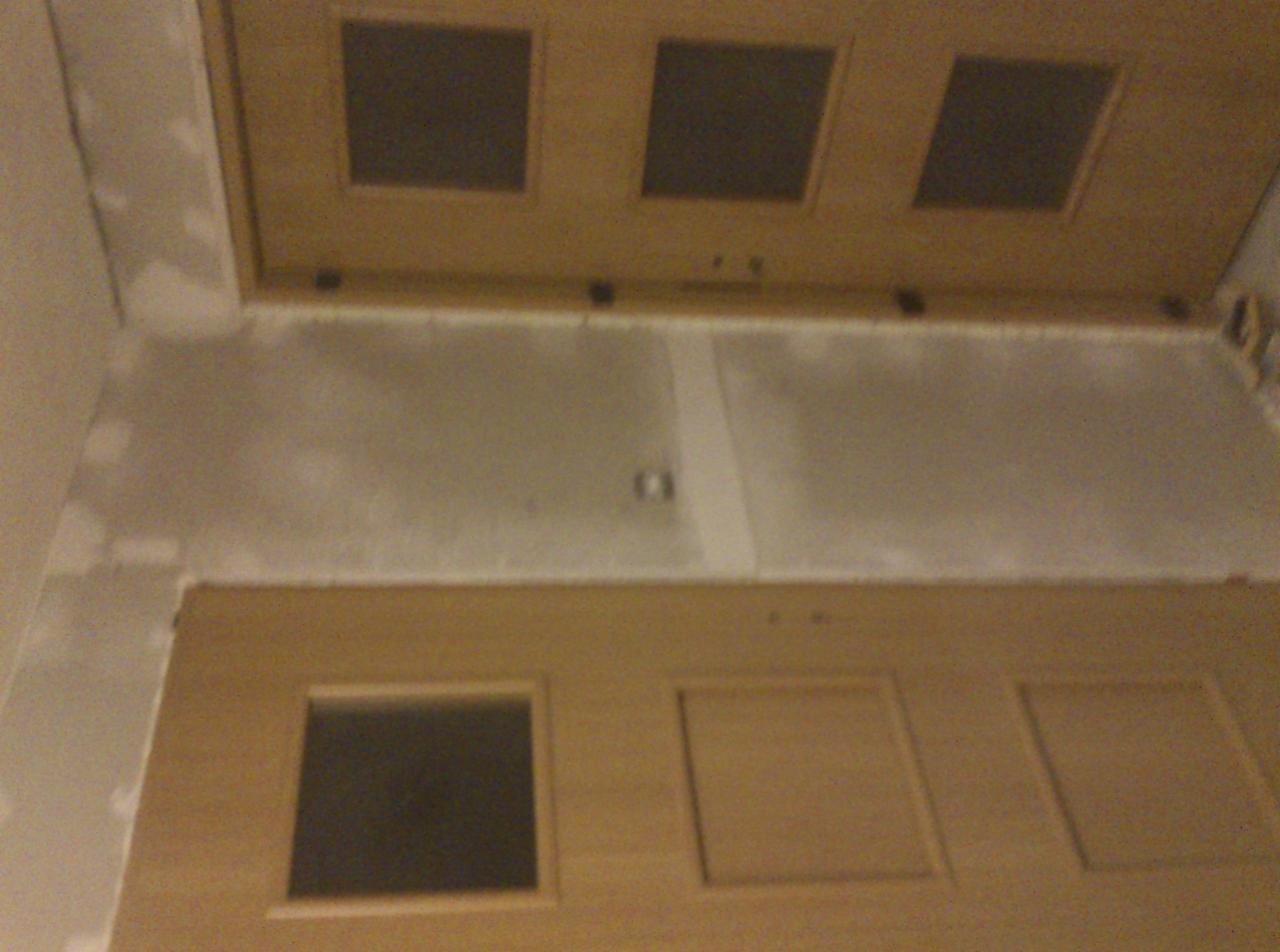 Sufit z zamontowaną płytą kartonowo-gipsową z widocznymi łączeniami i otworami rewizyjnymi. Widok z dołu na sufit w trakcie prac wykończeniowych.