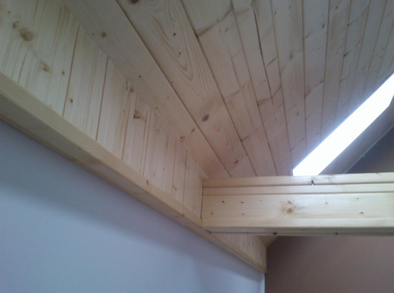 Drewniana boazeria na suficie i ścianie, jasne drewno z widocznymi słojami, wykończenie wnętrza w naturalnym stylu, sufit pod skosem z oświetleniem.