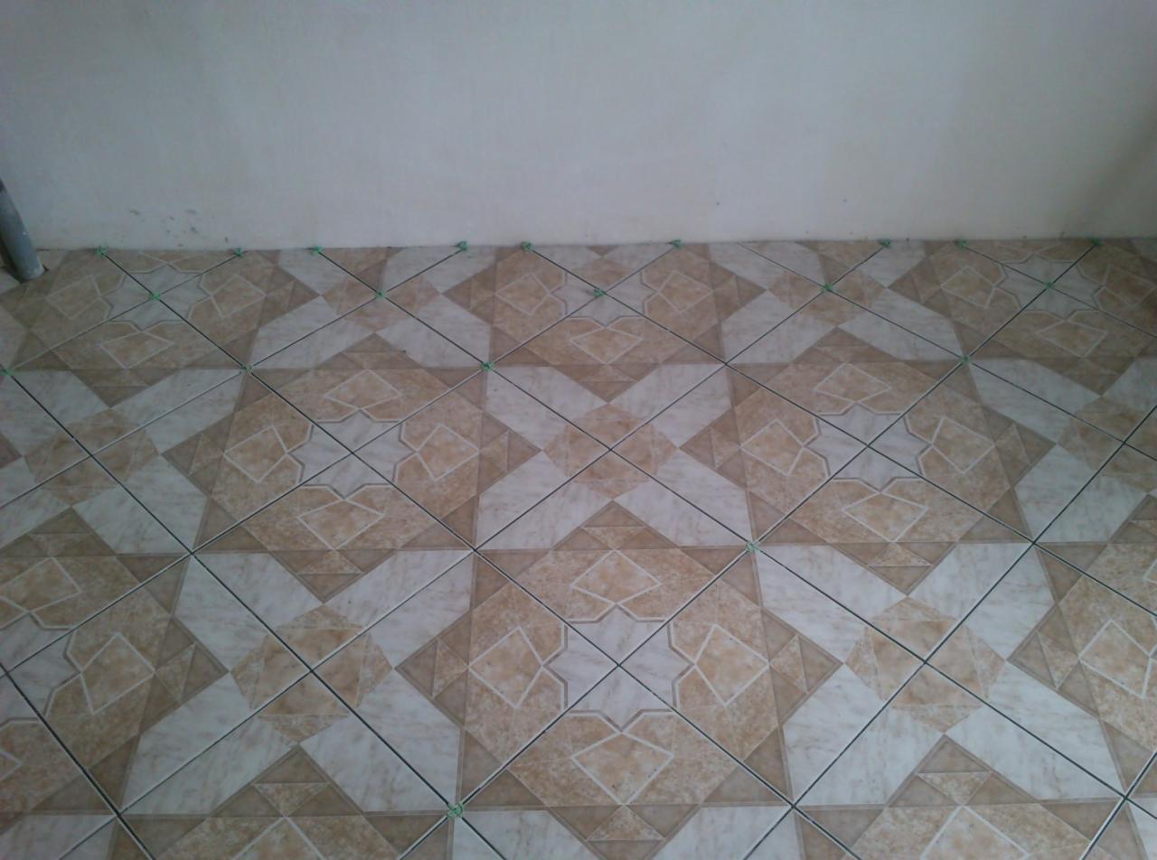 Ułożona podłoga z płytek w beżowo-białe wzory, widoczne zielone krzyżyki dystansowe, dolna część ściany. Ukończony etap prac wykończeniowych.