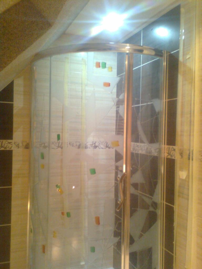 Nowoczesna kabina prysznicowa z dekoracyjną szybą i chromowanymi elementami wykończeniowymi, dopasowana do aranżacji łazienki z mozaiką.