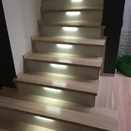 Bielone jesionowe stopnie schodów z białymi podstopnicami i wbudowanym oświetleniem LED na każdym stopniu, widok z dołu.