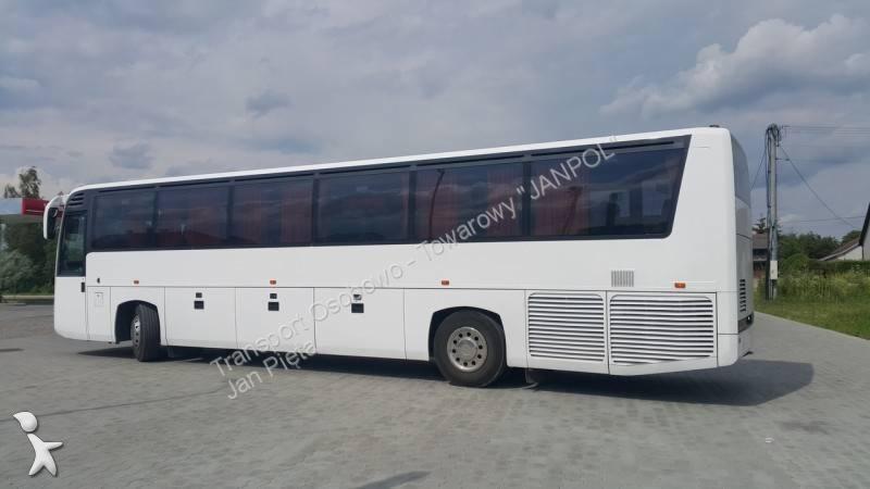 Biały autokar turystyczny z przyciemnianymi szybami, zaparkowany na szarym placu, widok z boku.