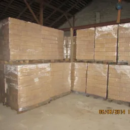 Składowane, owinięte folią palety z brykietem drzewnym w magazynie z drewnianą konstrukcją dachu. Widoczne datowanie zdjęcia w prawym dolnym rogu.