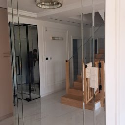 FHU Inny Wymiar Szkła Justyna Ługowska - Eleganckie lustro ścienne z fazowanych paneli w nowoczesnym wnętrzu. Widoczne odbicie schodów i drzwi przesuwnych, podkreślające przestronność i unikalny design.
