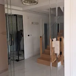 Eleganckie lustro ścienne z fazowanych paneli w nowoczesnym wnętrzu. Widoczne odbicie schodów i drzwi przesuwnych, podkreślające przestronność i unikalny design.