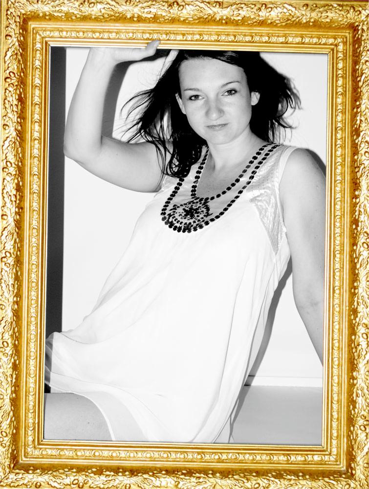 Portret kobiety w białej sukience i naszyjniku z czarnymi koralikami, pozującej w złotej, zdobionej ramie.