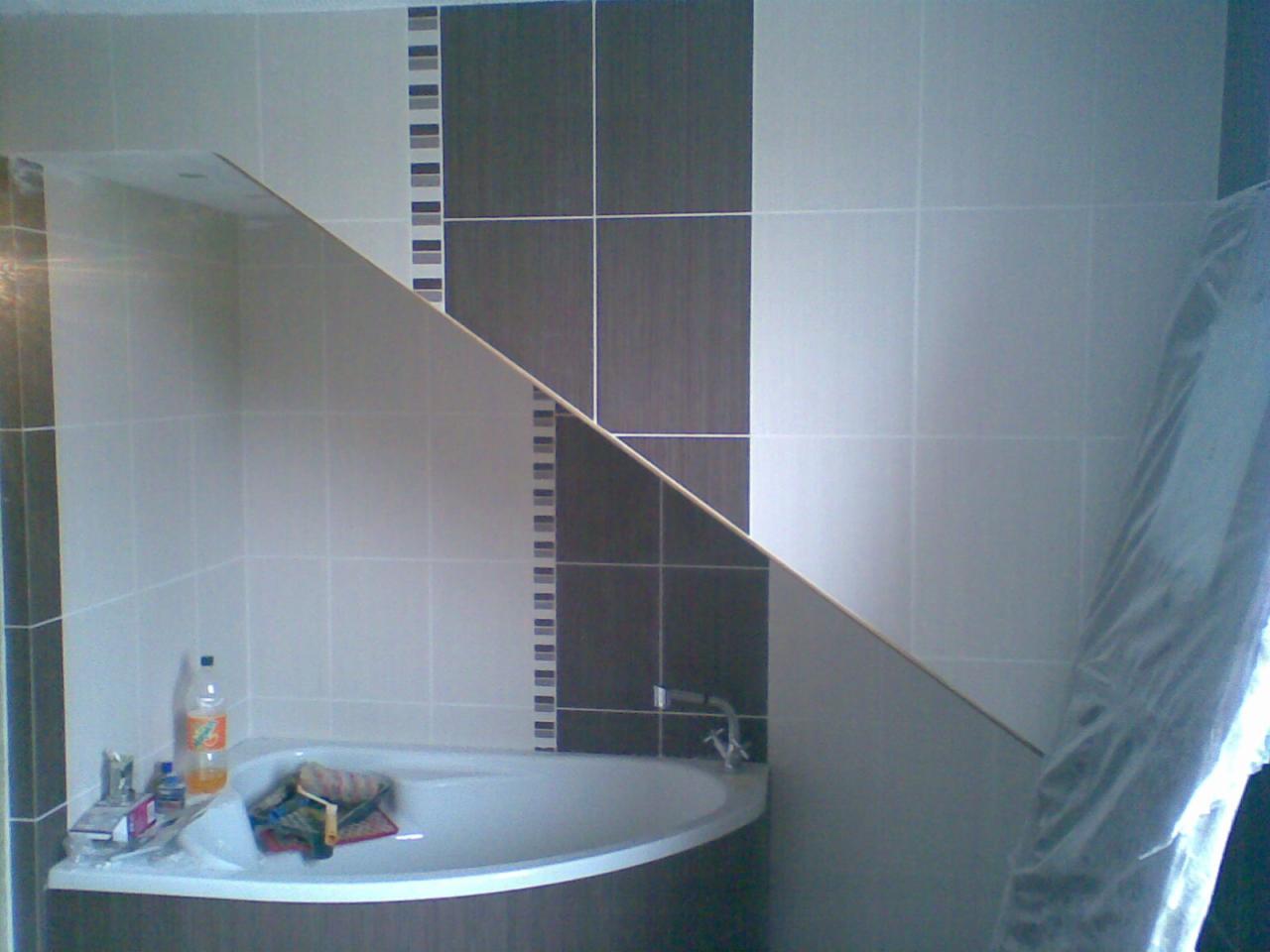 Wykończona łazienka z narożną wanną i glazurą w odcieniach bieli, szarości i brązu. Widoczne akcesoria łazienkowe i fragment zabezpieczonej folią strefy.