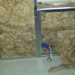 Ocieplenie poddasza wełną mineralną, widoczne profile montażowe i fragment instalacji elektrycznej. Detal wykończenia, surowy stan.